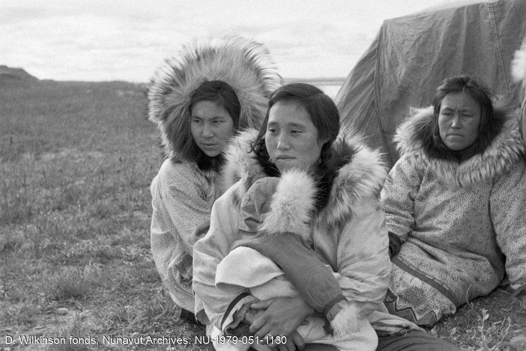 Femmes des éleveurs inuits, assises devant la tente, regardant les hommes rassembler le troupeau. Centre de rassemblement des rennes, delta du Mackenzie. Août 1955. 