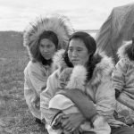 Femmes des éleveurs inuits, assises devant la tente, regardant les hommes rassembler le troupeau. Centre de rassemblement des rennes, delta du Mackenzie. Août 1955. 